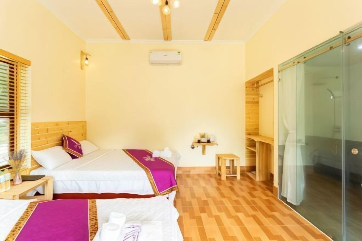 A hotel room with two beds, a wooden floor, a glass shower enclosure, and a small wooden stool.