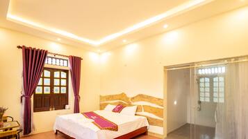 A bedroom with a bed, a glass shower enclosure, and a window with curtains.