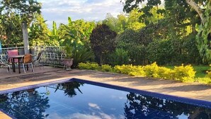 A rectangular swimming pool with a tiled edge, surrounded by a garden with various plants and a metal fence. - Balsora Hotel Boutique (La Tebaida)
