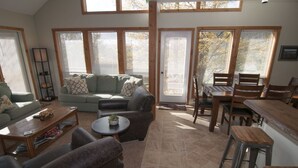Uma sala de estar ampla com sofá, poltronas, mesa de centro e mesa de jantar com cadeiras.