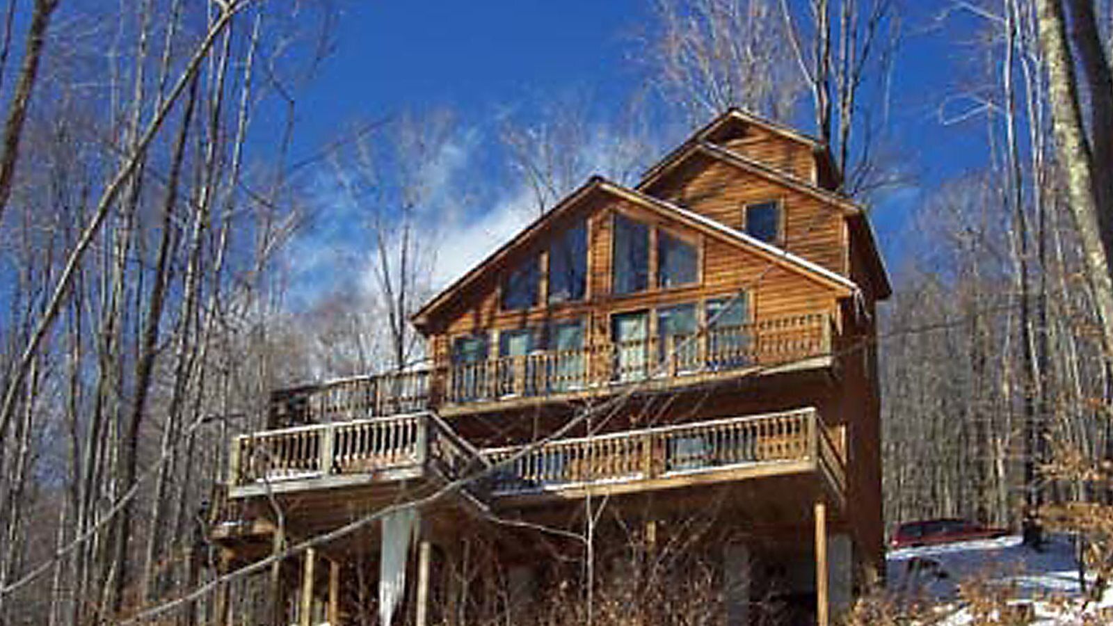 A two-story wooden cabin with a balcony, surrounded by trees.