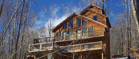 A two-story wooden cabin with a balcony, surrounded by trees.