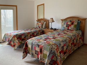 A bedroom with two single beds, a nightstand with a lamp, and a window with blinds. - Zigadeaux (Davis)