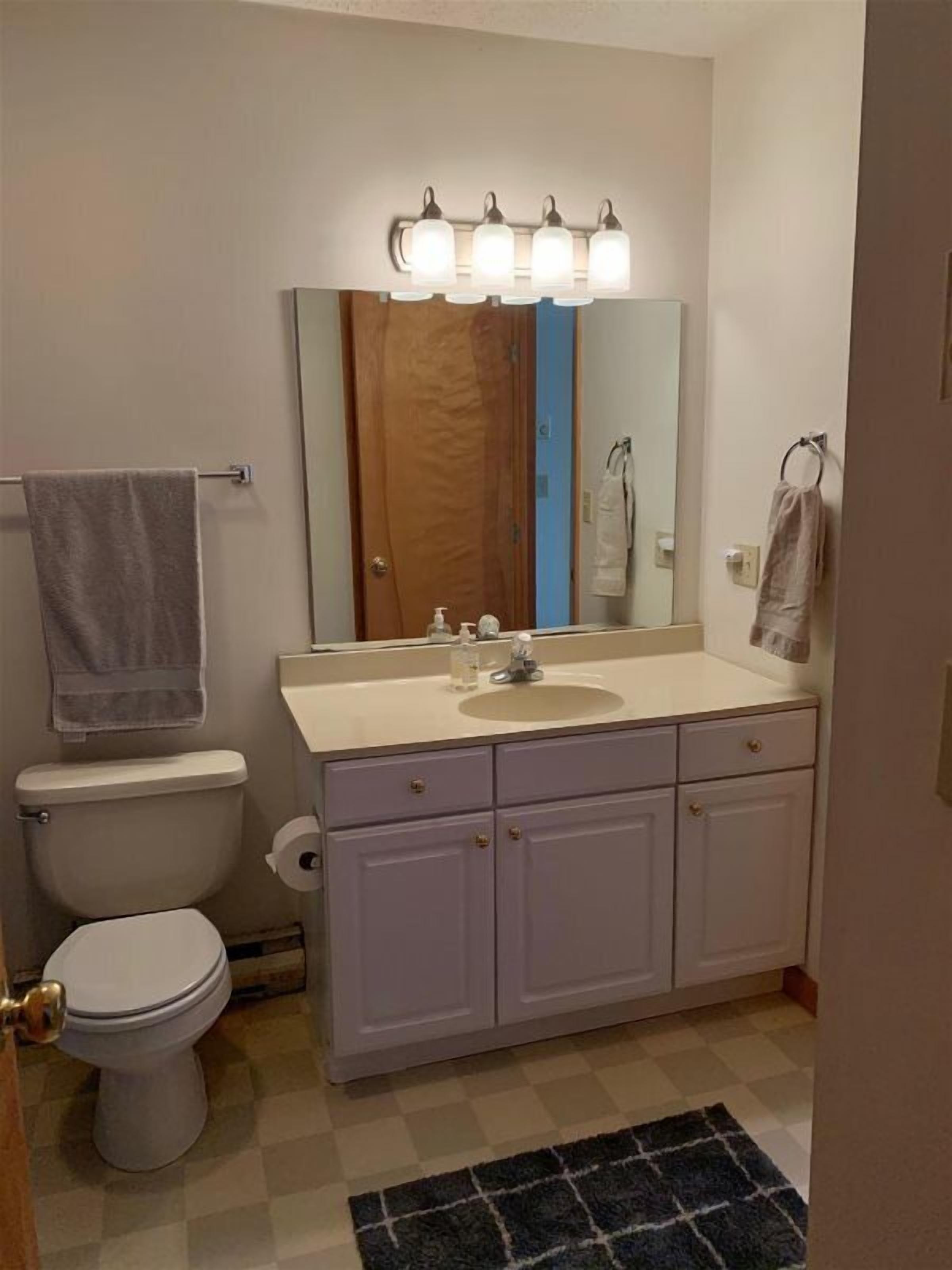 A bathroom with a toilet, sink, mirror, and towel rack.