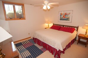 A bedroom with a bed, two bedside lamps, a ceiling fan, a window, and a painting on the wall.