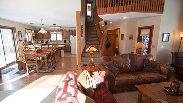 A spacious living room with a large brown leather sofa, a patterned red couch, and a wooden coffee table. A staircase leads to an upper level with a wooden railing.