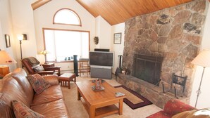 A cozy living room with a stone fireplace, leather sofa, wooden coffee table, and a television.