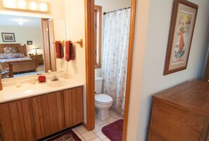 Ein Badezimmer mit Holzwaschtisch, Spiegel, Toilette und Duschvorhang.