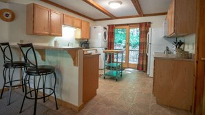 A compact kitchen with wooden cabinets, a central island with stools, a washing machine, and a dining area with a view through a glass door. - White Deer (Davis)