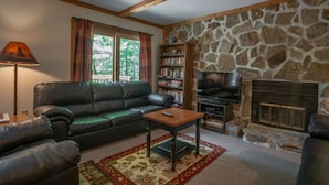 A cozy living room with a stone fireplace, a leather sofa, a coffee table, and a bookshelf filled with books. - White Deer (Davis)