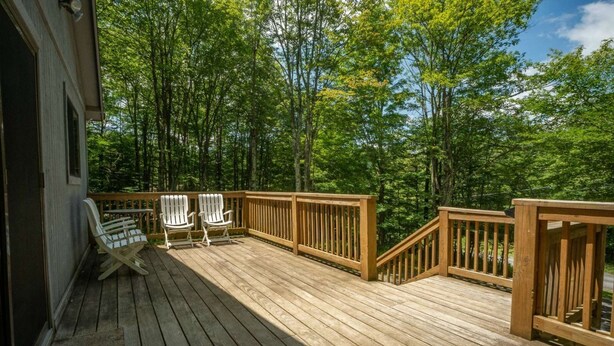A wooden deck with two Adirondack chairs and a staircase leading to a higher level. - White Deer (Davis)