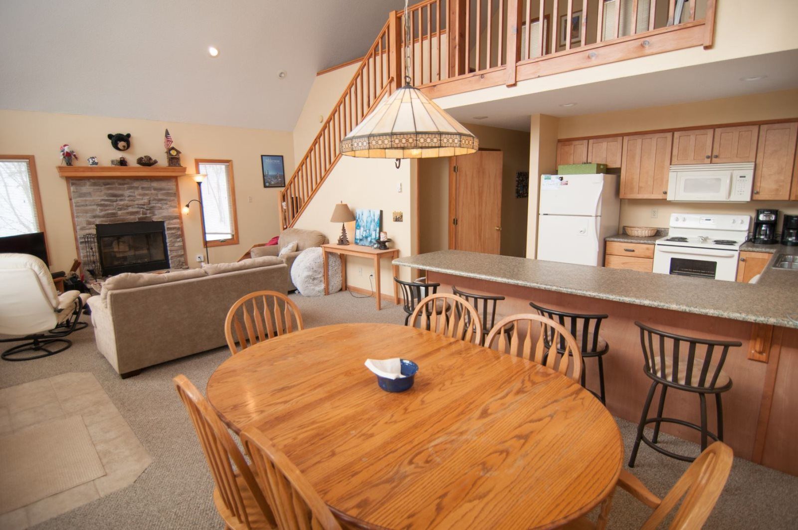 Una sala de estar acogedora con chimenea, un comedor con mesa y sillas de madera, y una cocina con armarios de madera y un microondas.
