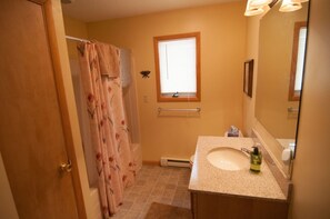 A bathroom with a shower curtain, a window with blinds, a sink with a mirror, and a towel rack. - Tranquility Base (Davis)