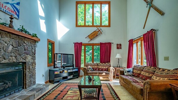 A spacious living room with a stone fireplace, a television, and a large window with curtains. - White Diamond (Davis)