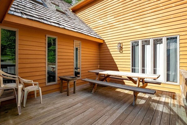 A wooden deck with a picnic table and chairs, large windows, and a covered area.