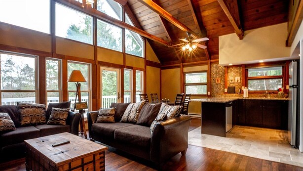 A spacious living room with a large sofa, a wooden coffee table, and a fireplace. There is a kitchen area with a refrigerator and a countertop. - Valley View Lodge (Davis)