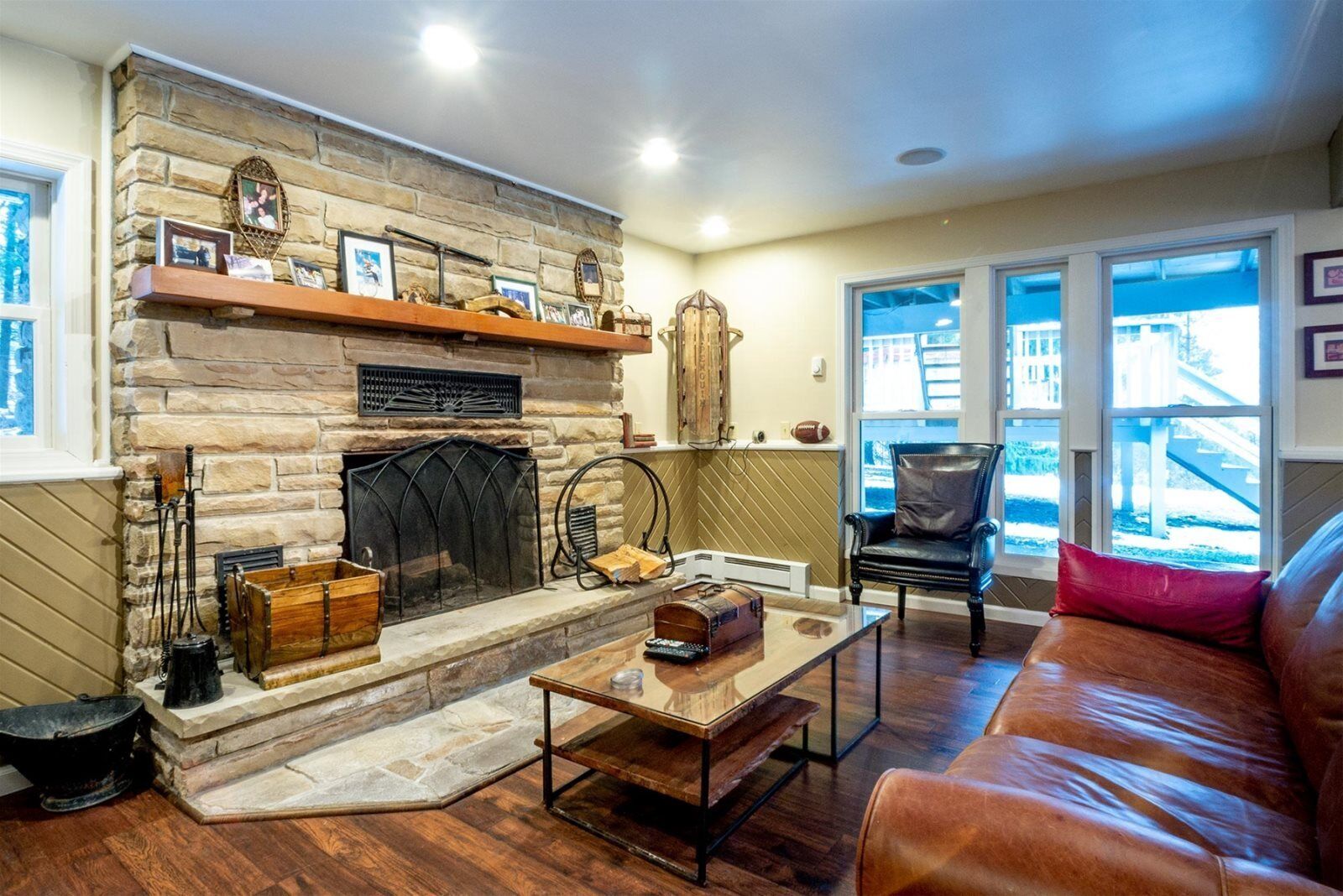 A cozy living room with a stone fireplace, leather furniture, and large windows offering a view of the outside.