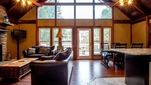A spacious living room with a fireplace, a comfortable sofa, a dining area with a table and chairs, and large windows allowing natural light. - Valley View Lodge (Davis)