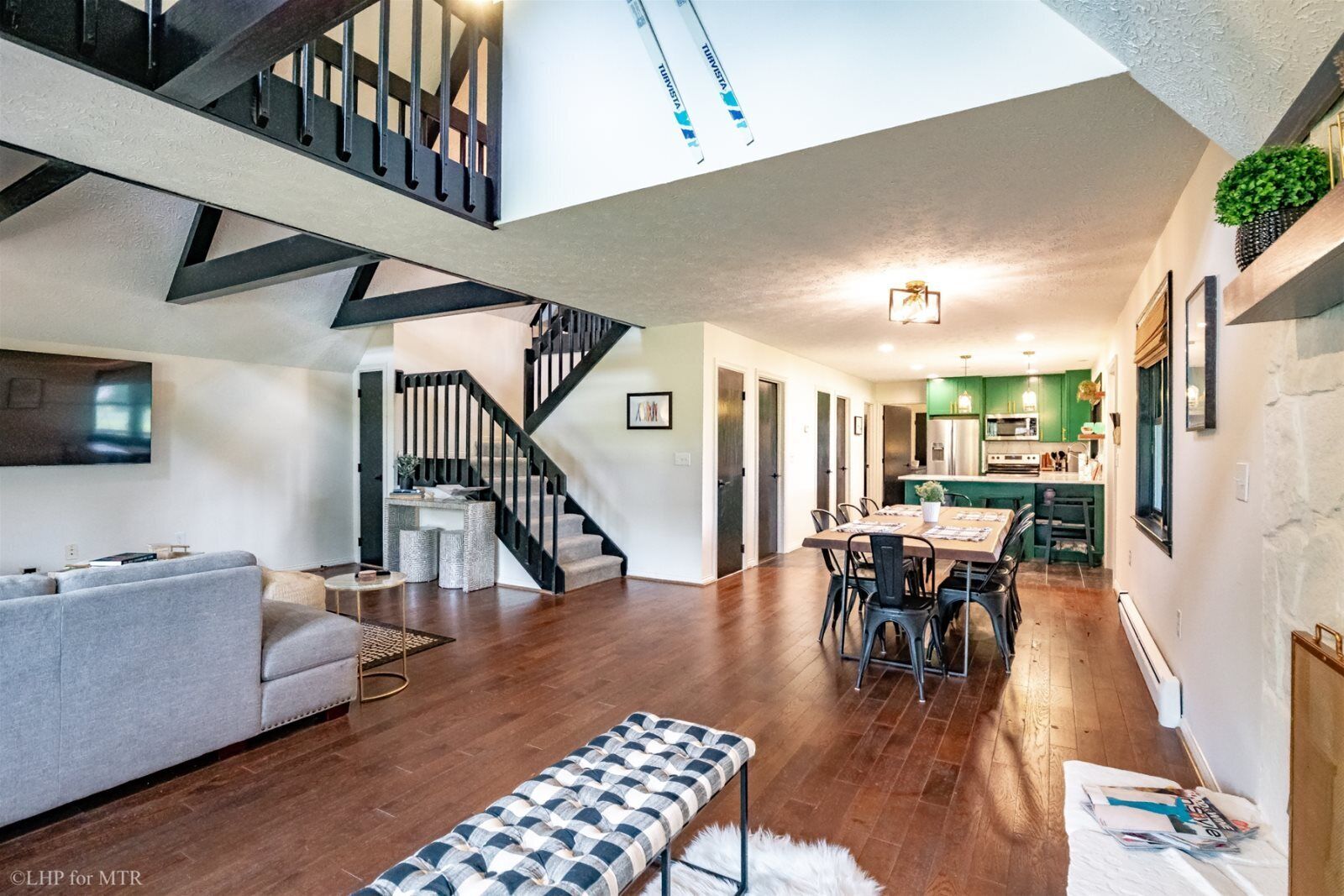 A spacious living area with a staircase, a dining table, and a kitchen in the background.