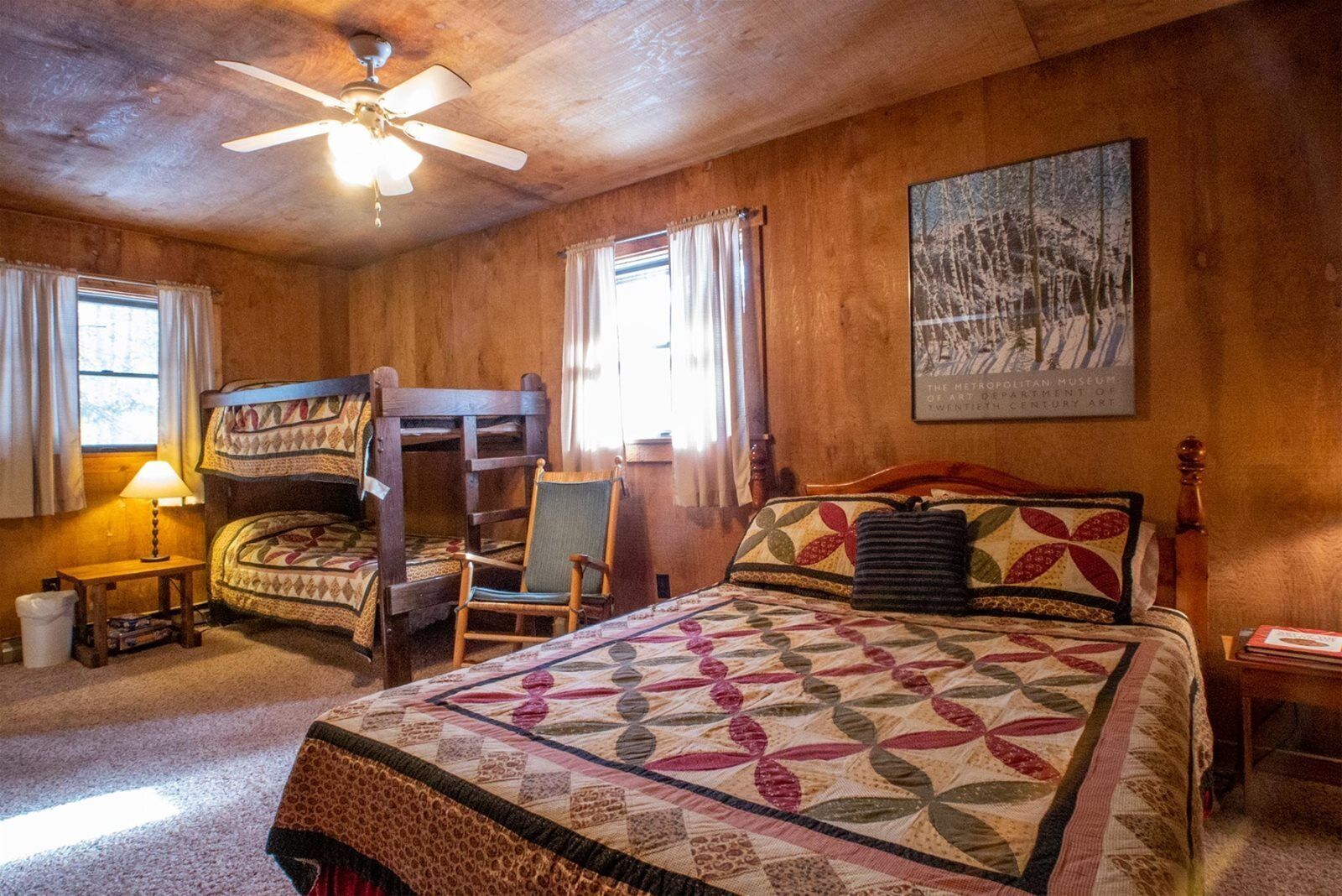 A cozy room with a bunk bed, a single bed, a chair, a lamp, and a painting on the wall.
