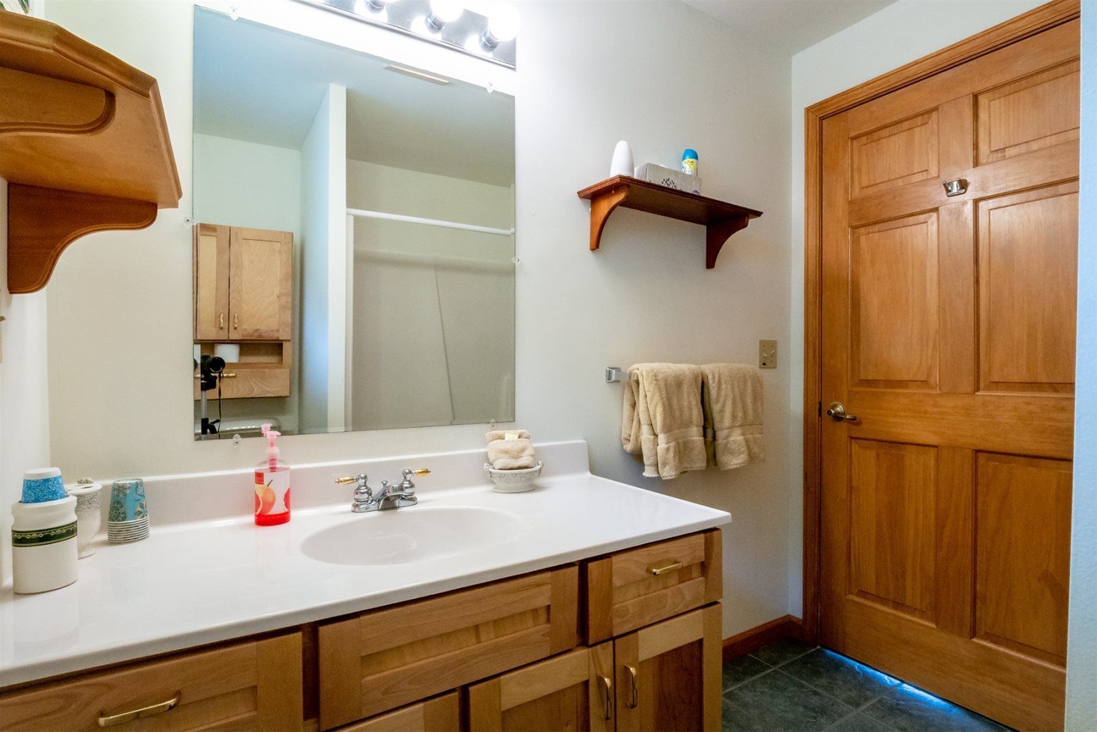 A bathroom with a white sink, wooden cabinets, a mirror, a towel rack, and a wooden door.