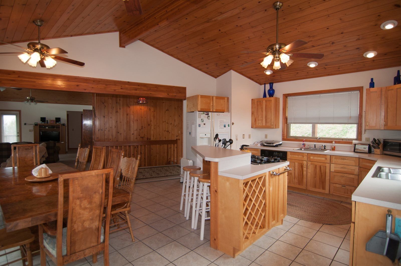 A spacious kitchen with wooden cabinets, a central island, and a dining area with chairs.