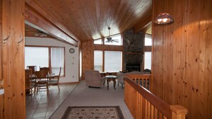 A wooden cabin interior with a dining area, a living room with a fireplace, and a balcony. - Sunset House (Davis)