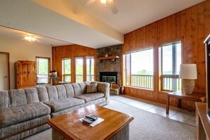 A cozy living room with a sectional sofa, a fireplace, a stone accent wall, and large windows offering a view.
