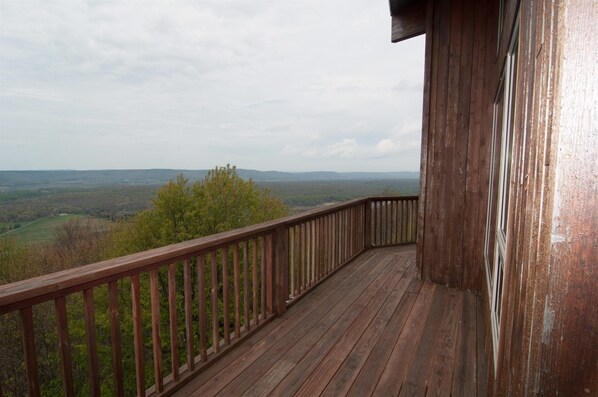 A wooden deck with a railing overlooking a forested landscape.