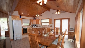 A spacious kitchen with wooden cabinets, a central island, and a dining area with wooden chairs. - Sunset House (Davis)