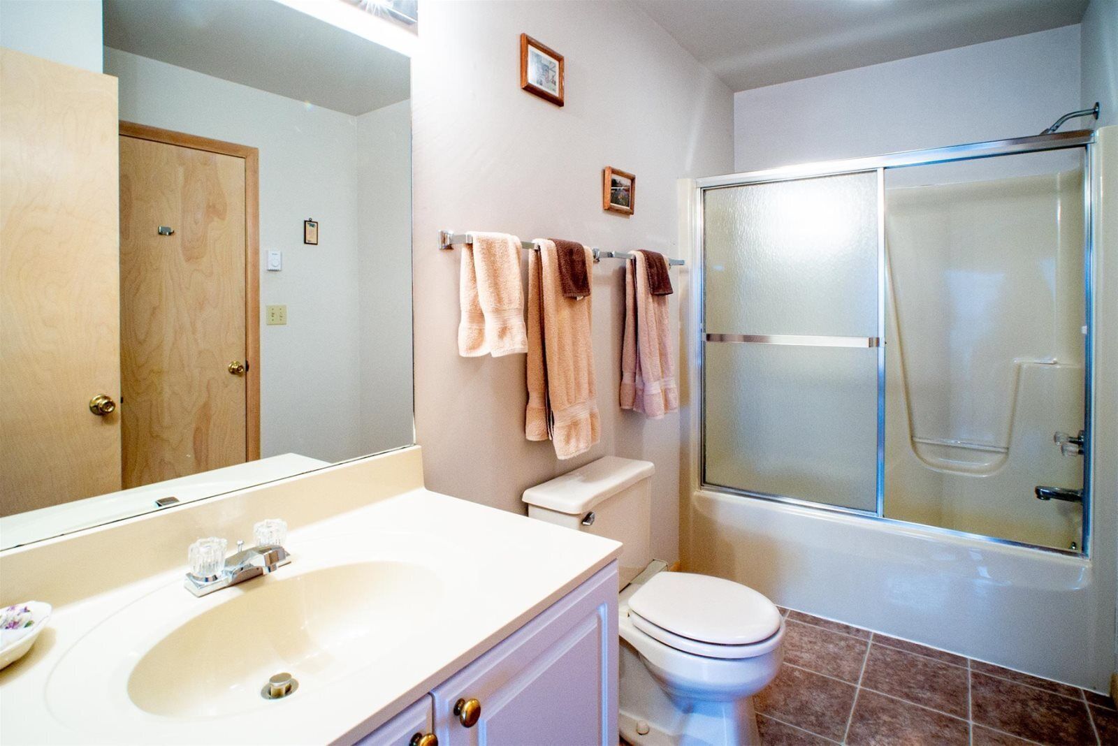 Une salle de bain avec un lavabo blanc, des toilettes et une douche fermée par des parois en verre.