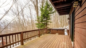 Una terraza de madera con un jacuzzi, rodeada de árboles y un paisaje nevado.