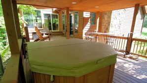 A hot tub on a wooden deck with chairs and a table, surrounded by a stone wall and glass doors.