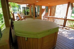 Una vasca idromassaggio su un pontile di legno, con sedie e un tavolo, circondata da un muro in pietra e porte in vetro.