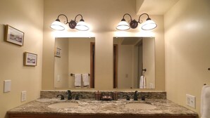 A bathroom with two sinks, a large mirror, and wall-mounted lighting.