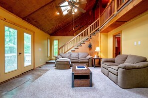 A spacious living room with a high ceiling, a staircase, and large windows. - Streamside Dreams (Davis)