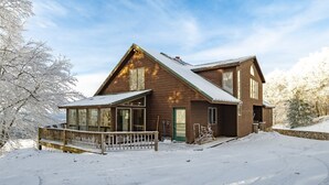 A wooden cabin with a snow-covered roof, large windows, and a wooden deck.