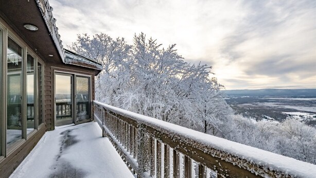 A snow-covered balcony with a view of a forest and distant landscape.