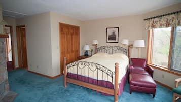 A bedroom with a wooden bed, a red chair, a stone wall, and a window with a curtain.