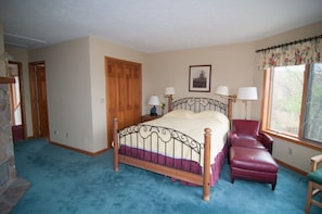 A bedroom with a wooden bed, a red chair, a stone wall, and a window with a curtain. - Spruce Lodge (Davis)