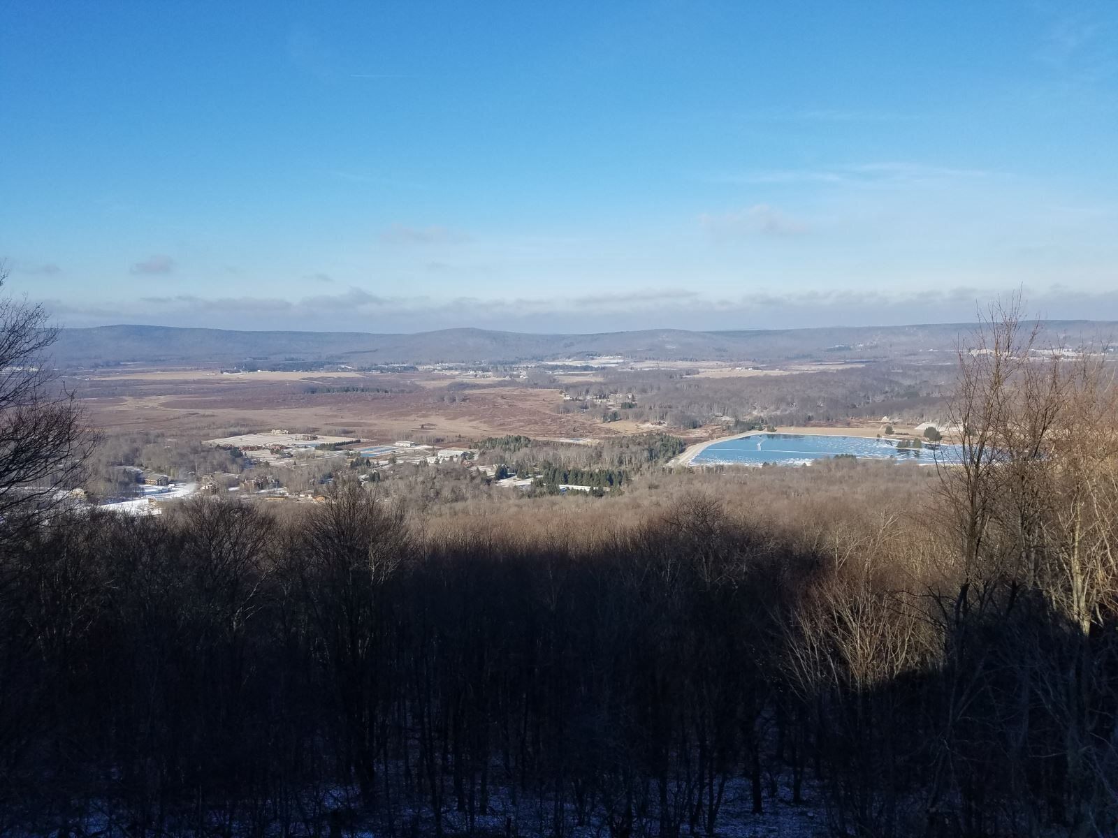 A panoramic view of a landscape with a lake, distant hills, and sparse vegetation.