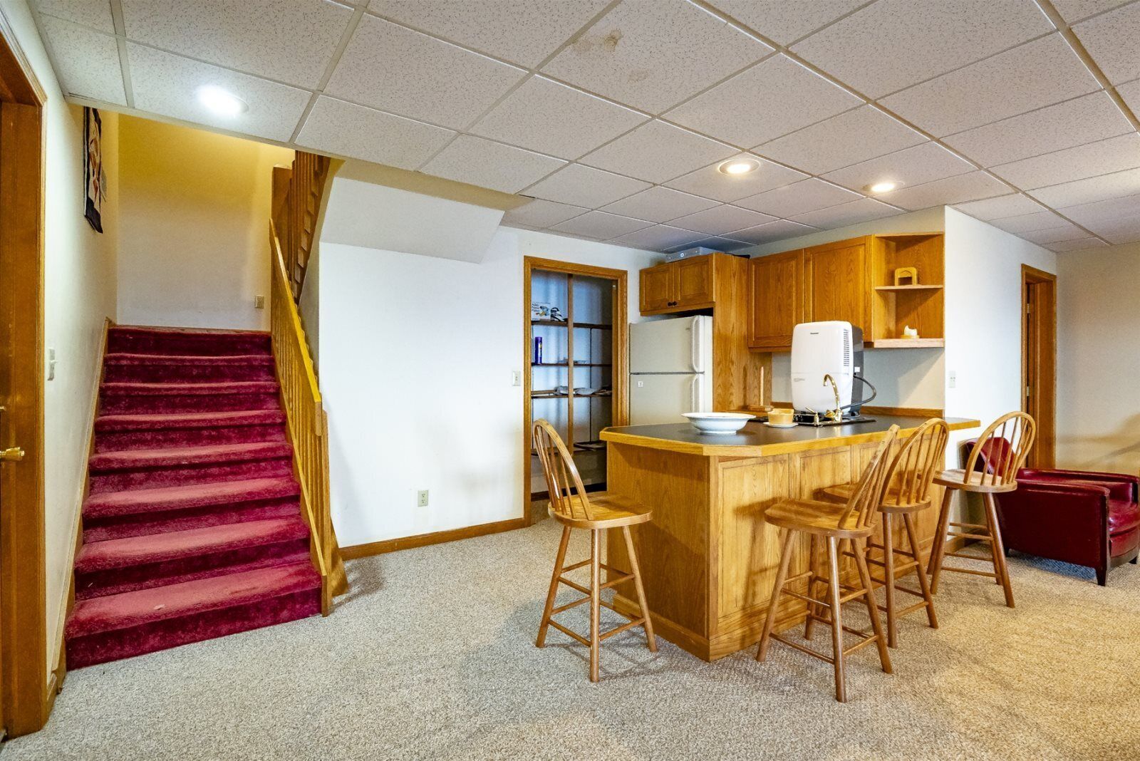 A kitchen with wooden cabinets, a central island with bar stools, a refrigerator, and a microwave.