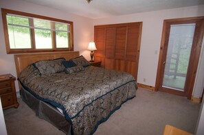 A bedroom with a large bed, a wooden headboard, a nightstand, a lamp, a wardrobe, and a door with a window.