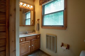 Un baño con armarios de madera, un tocador con espejo, una ventana con vistas a árboles y un calentador instalado en la pared.