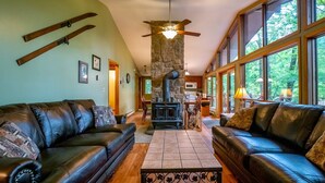 A cozy living room with leather sofas, a stone fireplace, and large windows offering a view of the outdoors. - Our Greyt Escape (Davis)