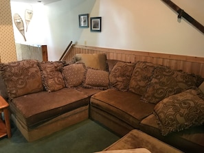 A corner sofa with multiple cushions, a wooden headboard, and a small table. - Northwoods H5 (Davis)