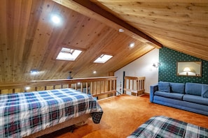 A cozy attic bedroom with wooden beams, a sloped ceiling, and a blue sofa. - Northwoods H5 (Davis)