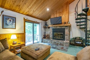 A cozy living room with a stone fireplace, wooden ceiling, and a television mounted above it. - Northwoods H5 (Davis)