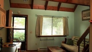 Um quarto aconchegante com teto de madeira, uma mesa de jantar com cadeiras, um sofá e uma janela com cortinas.