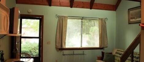 A cozy room with a wooden ceiling, a dining table with chairs, a sofa, and a window with curtains.